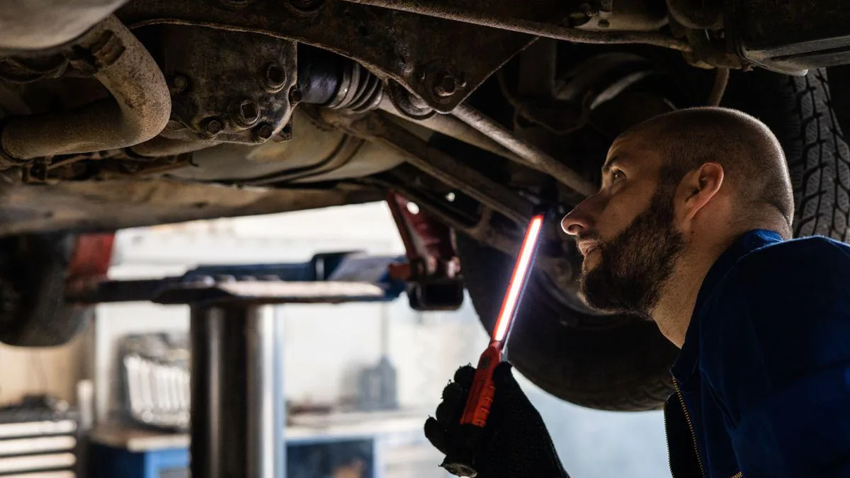 Mechanic in overalls inspecting undercarriage of car on a hoist with inspection light