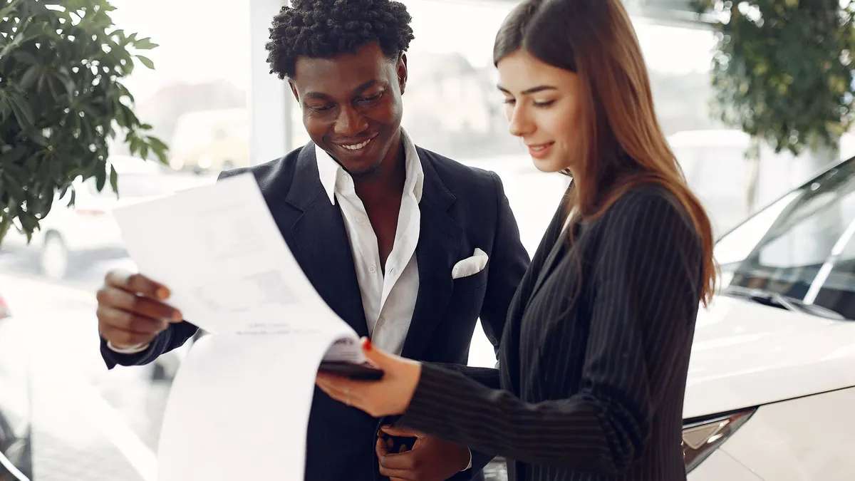 A car buyer and a salesperson reading a sale contract together in a dealership