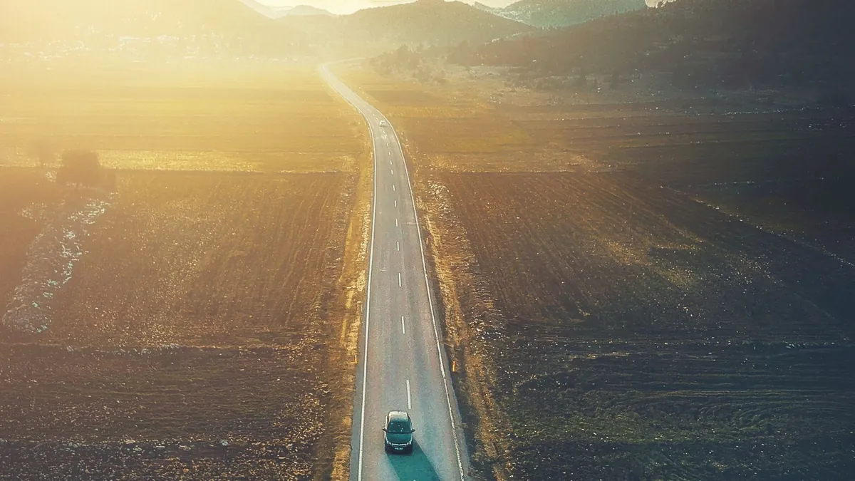 A car driving along a long country highway at sundown