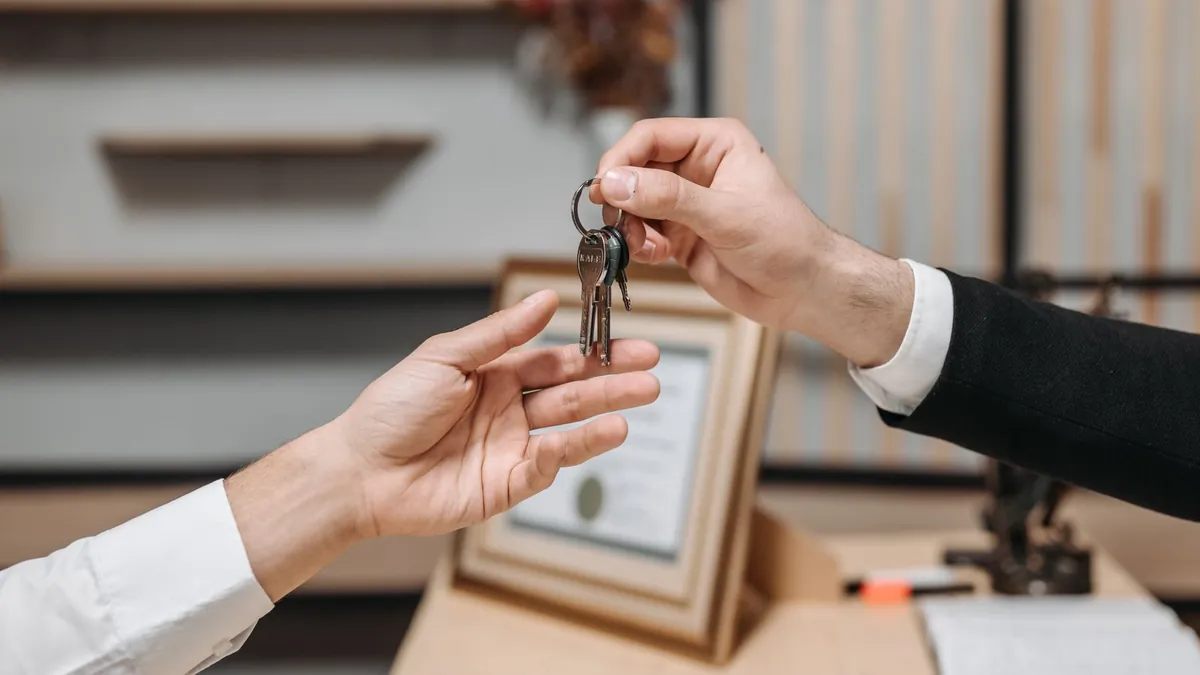 One person handing a set of car keys to another across a desk