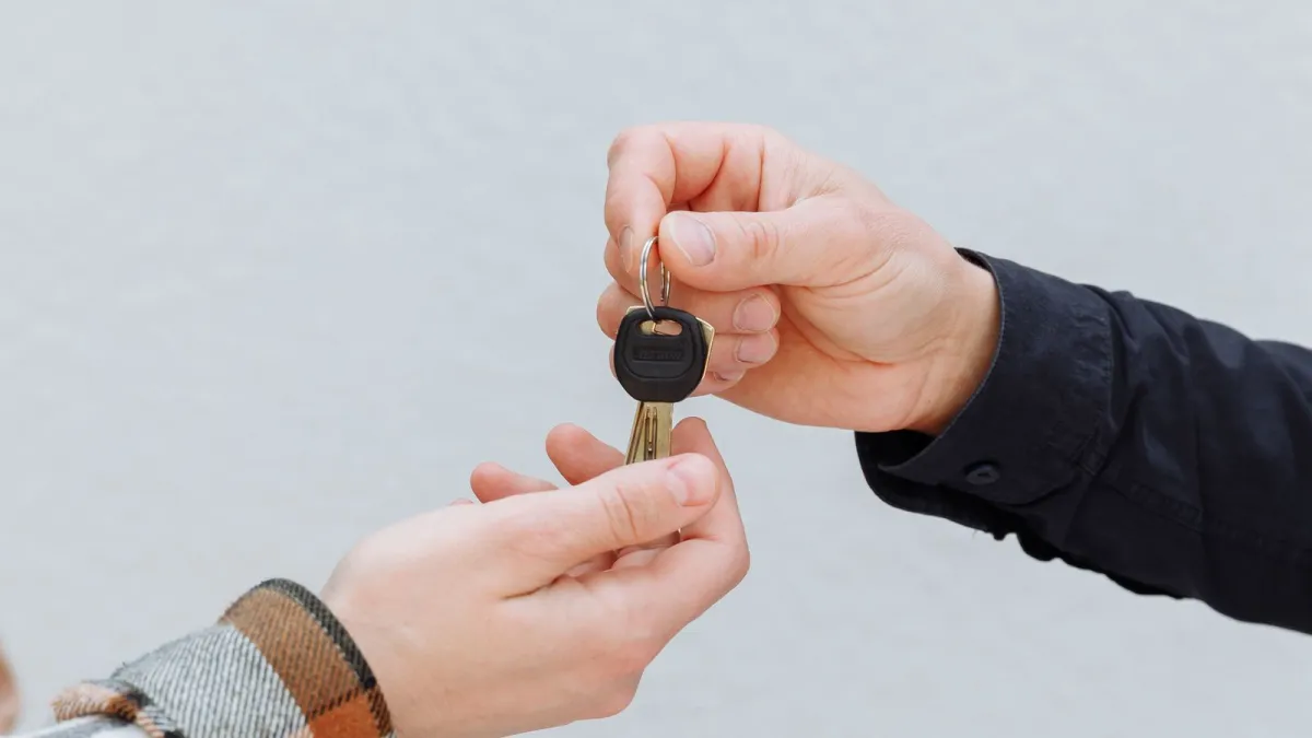 Two hands exchanging a car key above a signed contract