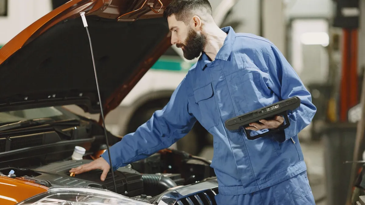 A mechanic holding a tablet while checking a car's engine bay