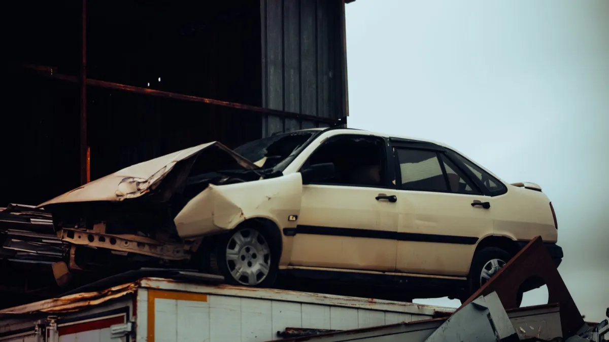 A sedan with a crushed front end resting on a pile of scrap