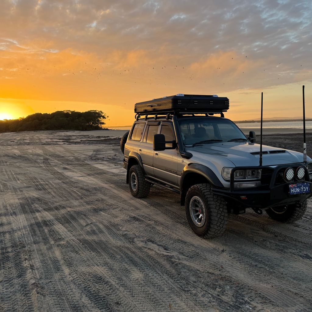 Four-wheel drive with a roof tent on the sand at sunset